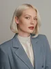 Krótko ostrzyżone blond włosy, elegancki marynarka, biała koszula.
